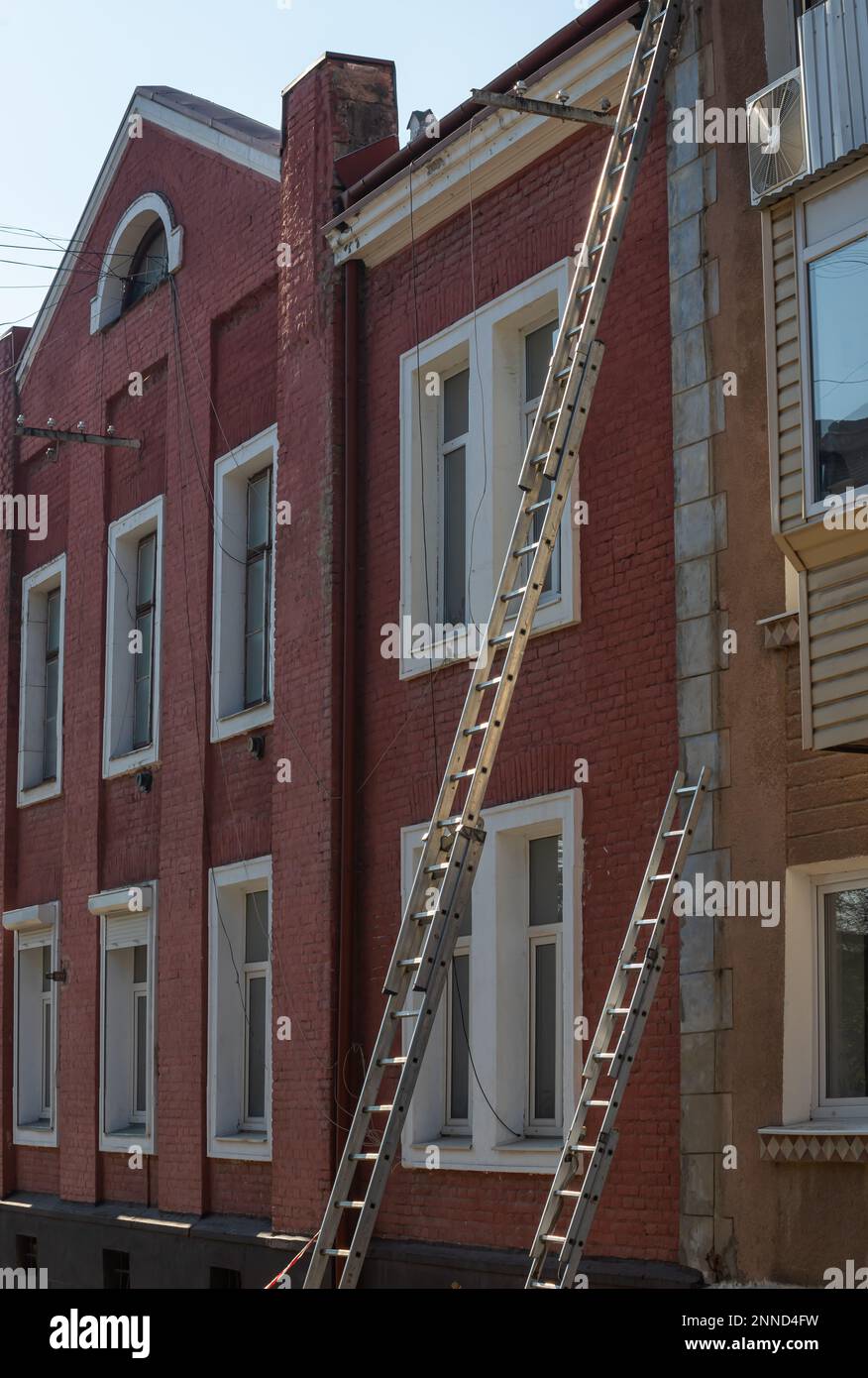 An extension ladder leans against the front of a multifamily housing building in preparation of roof repairs. Stock Photo