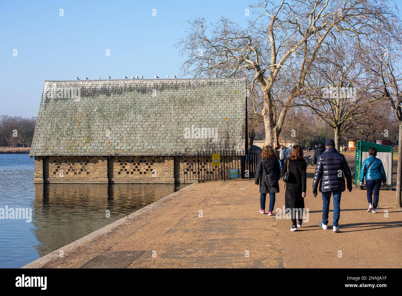 Strolling people and old boathouse by The Serpentine recreational lake on a sunny winter day in Hyde Park, London, England Stock Photo