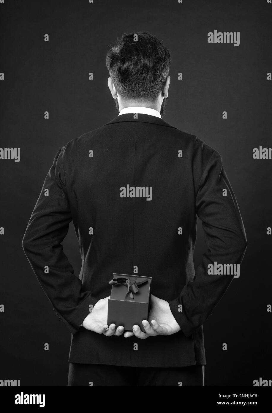 back view of man in tuxedo suit on black background with box. birthday