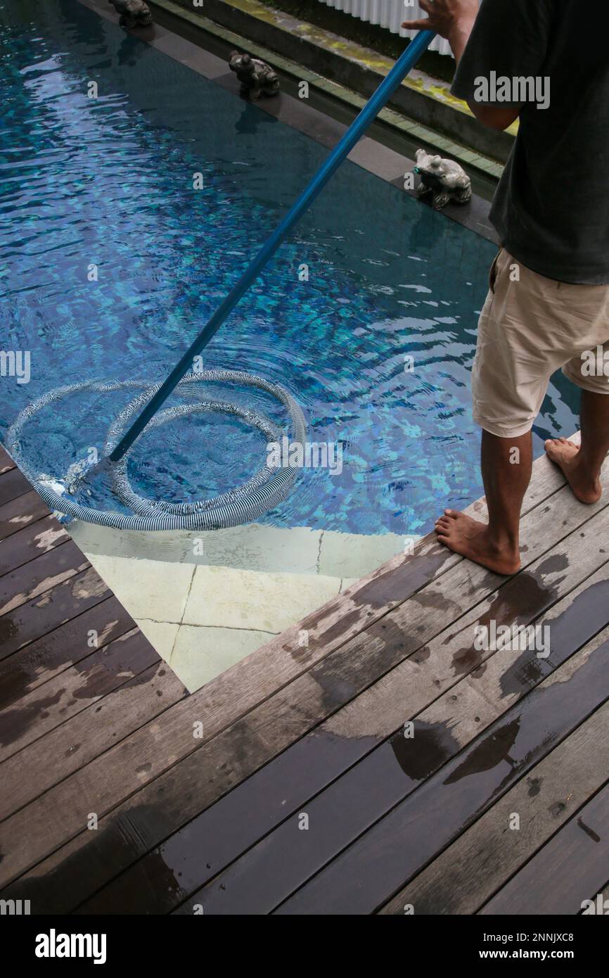 Man cleaning swimming pool with vacuum tube cleaner. Weekly pool