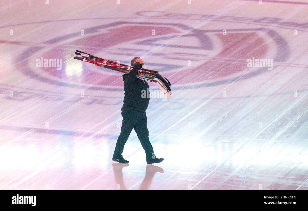 An Edmonton Oilers equipment manager carries sticks across the ice of