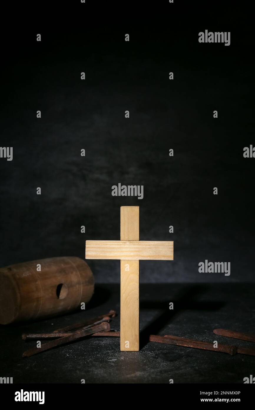 Wooden cross with nails and mallet on dark background, closeup. Good
