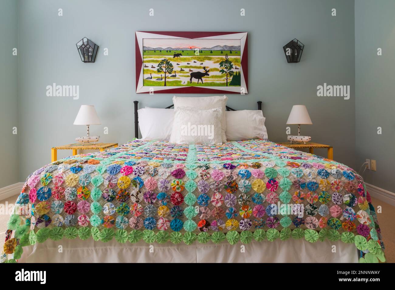 Queen size bed with black antique wrought iron headboard and colourful flowery motif quilt