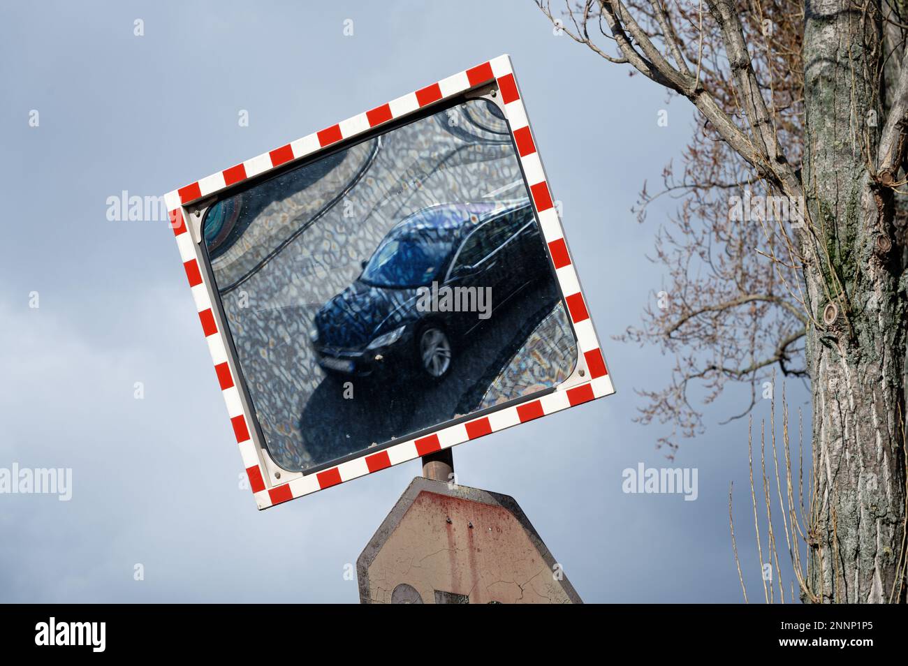a traffic mirror with red and white border reflects a car on a road Stock Photo