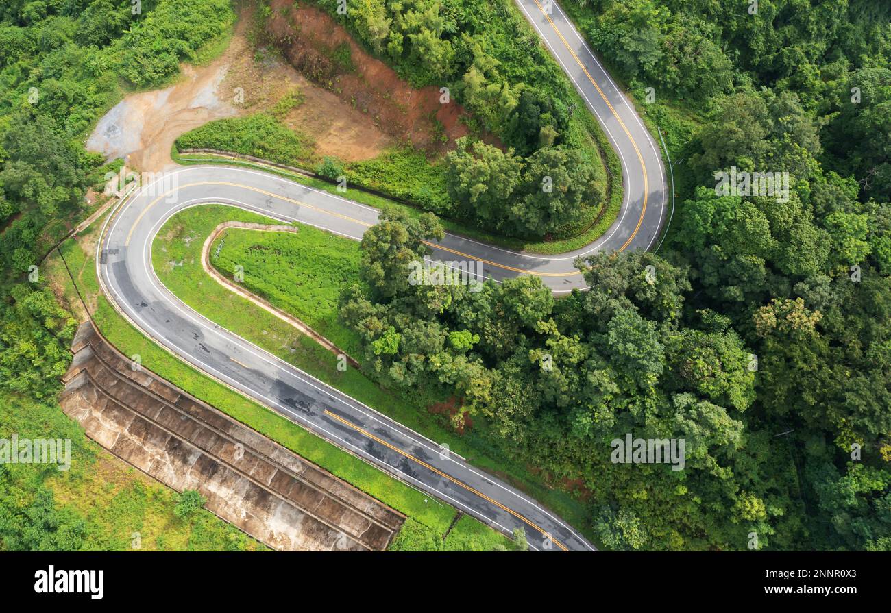 Aerial view drone fly over countryside road passing through the green forest and mountain in Thailand. Mountain winding zig zag road. Top aerial view Stock Photo