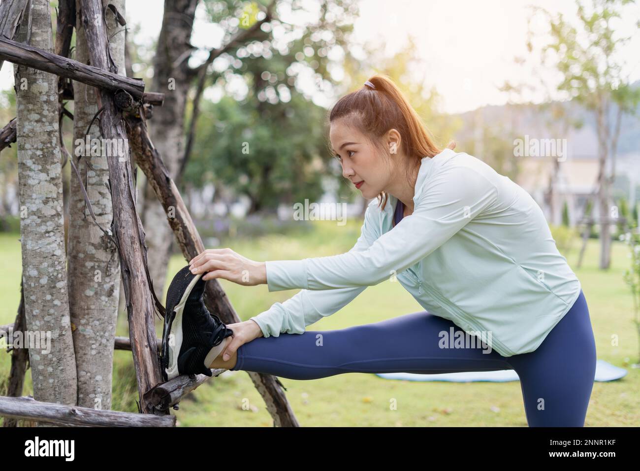 City life and Healthy lifestyle concept. Female athlete runner. Woman stretching her leg outside before running. Portrait of sporty woman doing hamstr Stock Photo