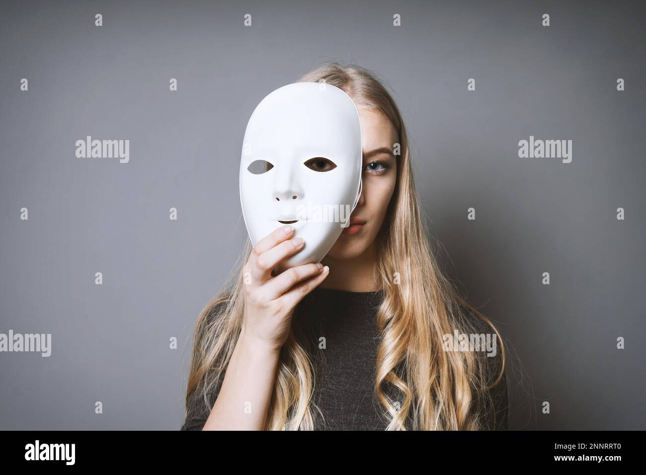 teen girl hiding her face behind mask - identity or personality concept Stock Photo