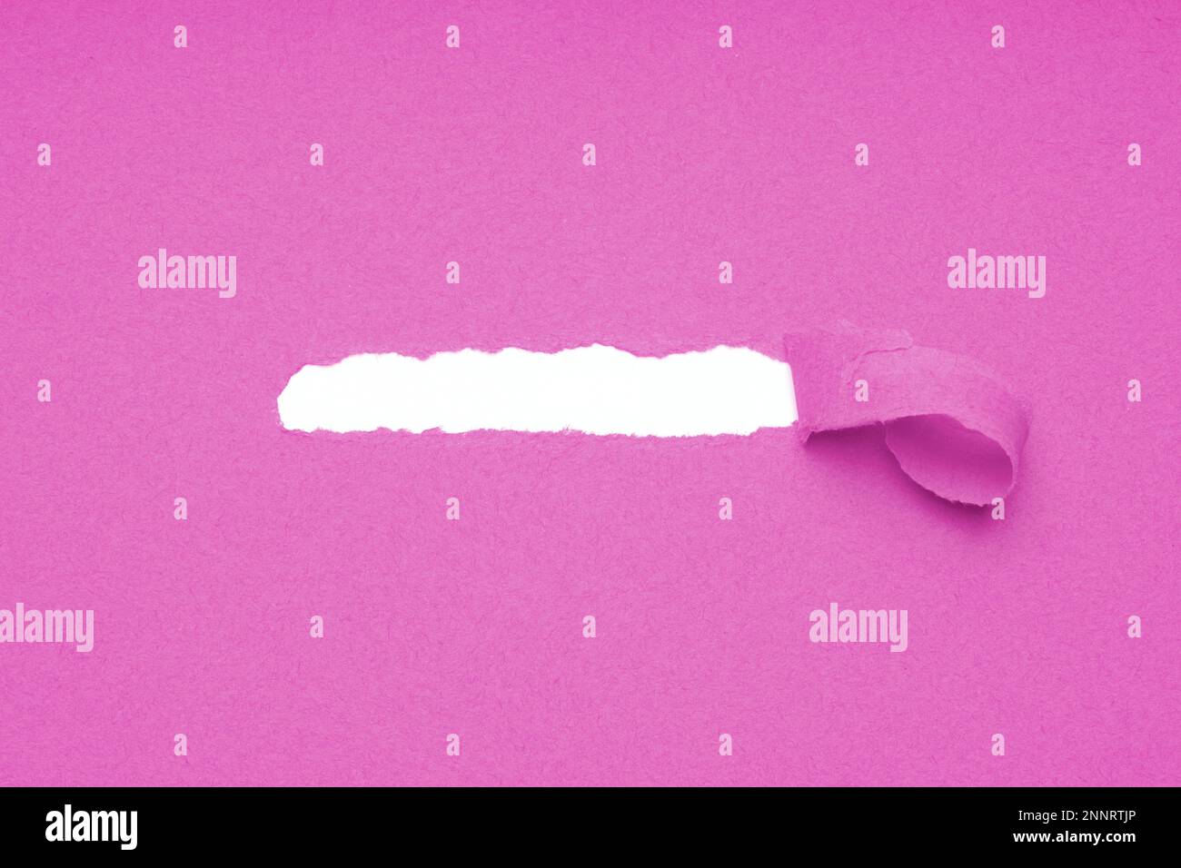 hole torn in pink paper background to reveal hidden copy space underneath Stock Photo