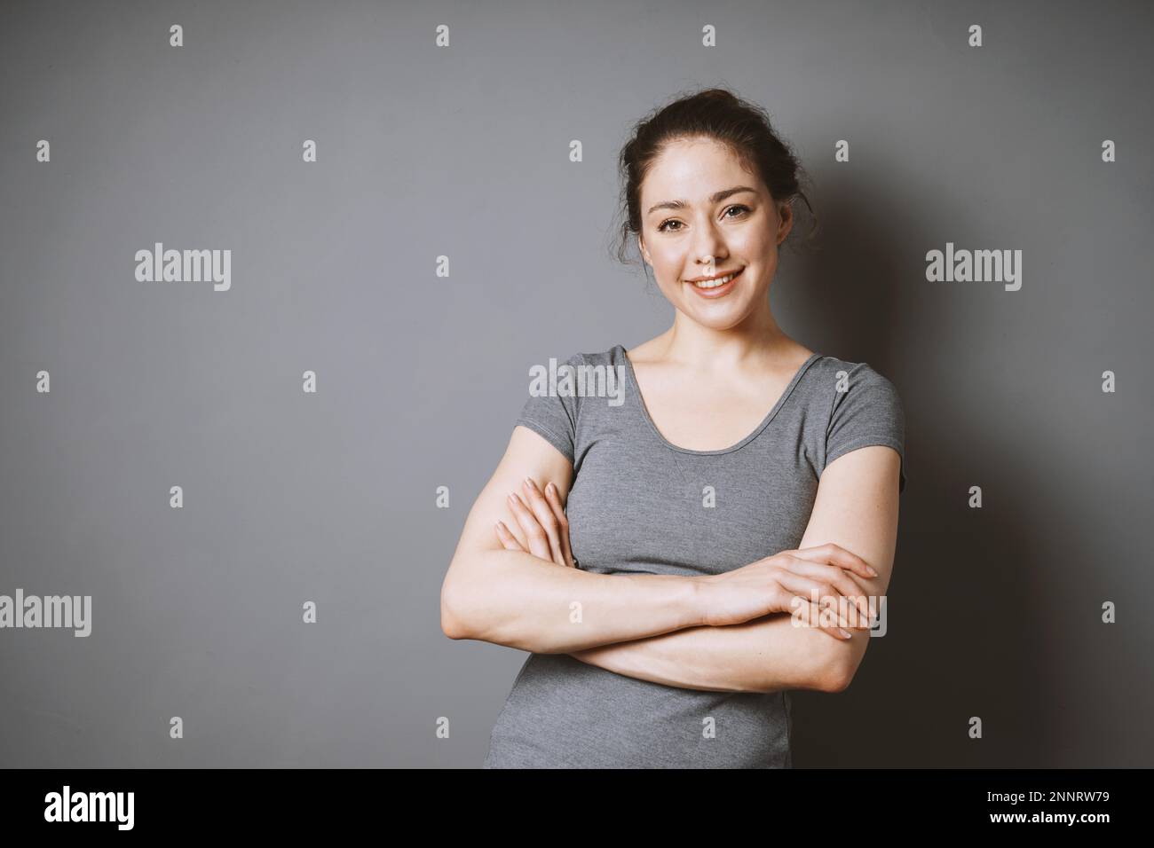 confident smiling young woman in her 20s with her arms folded against ...