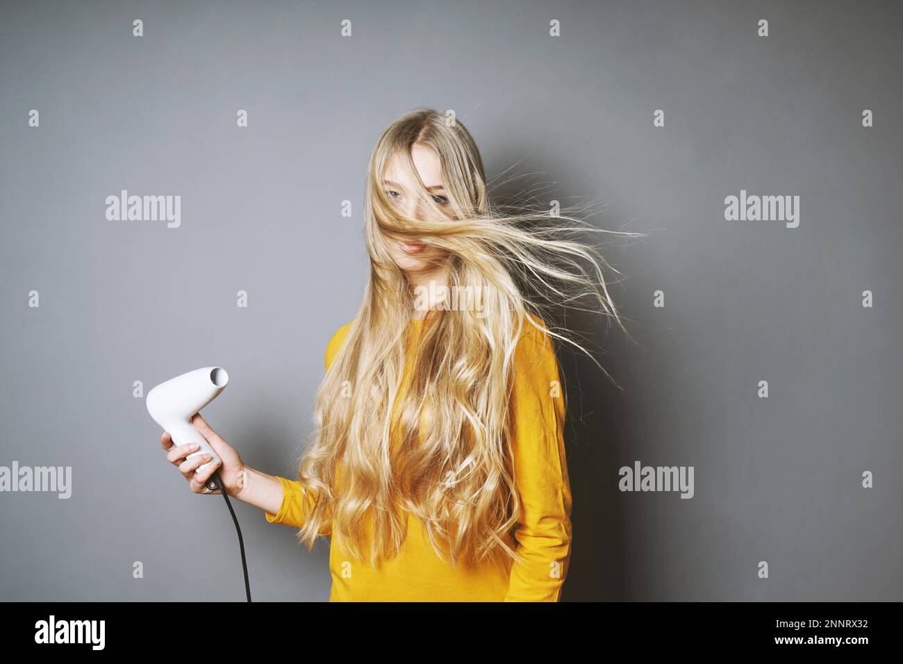 funny young blond woman blow-drying her long hair with blow dryer Stock ...