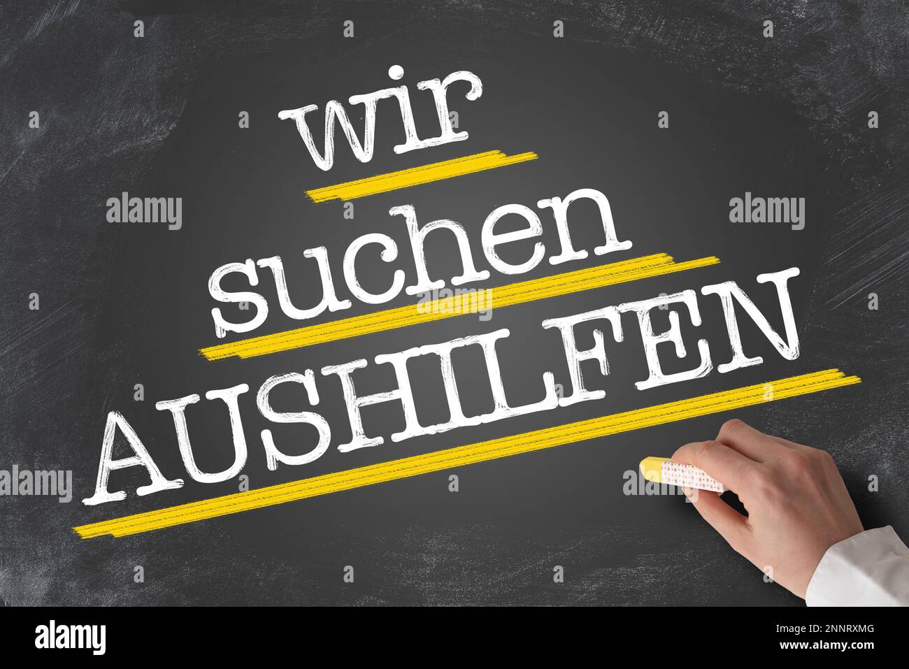 text WIR SUCHEN AUSHILFEN, German for Help Wanted, written on blackboard with hand holding piece of chalk Stock Photo