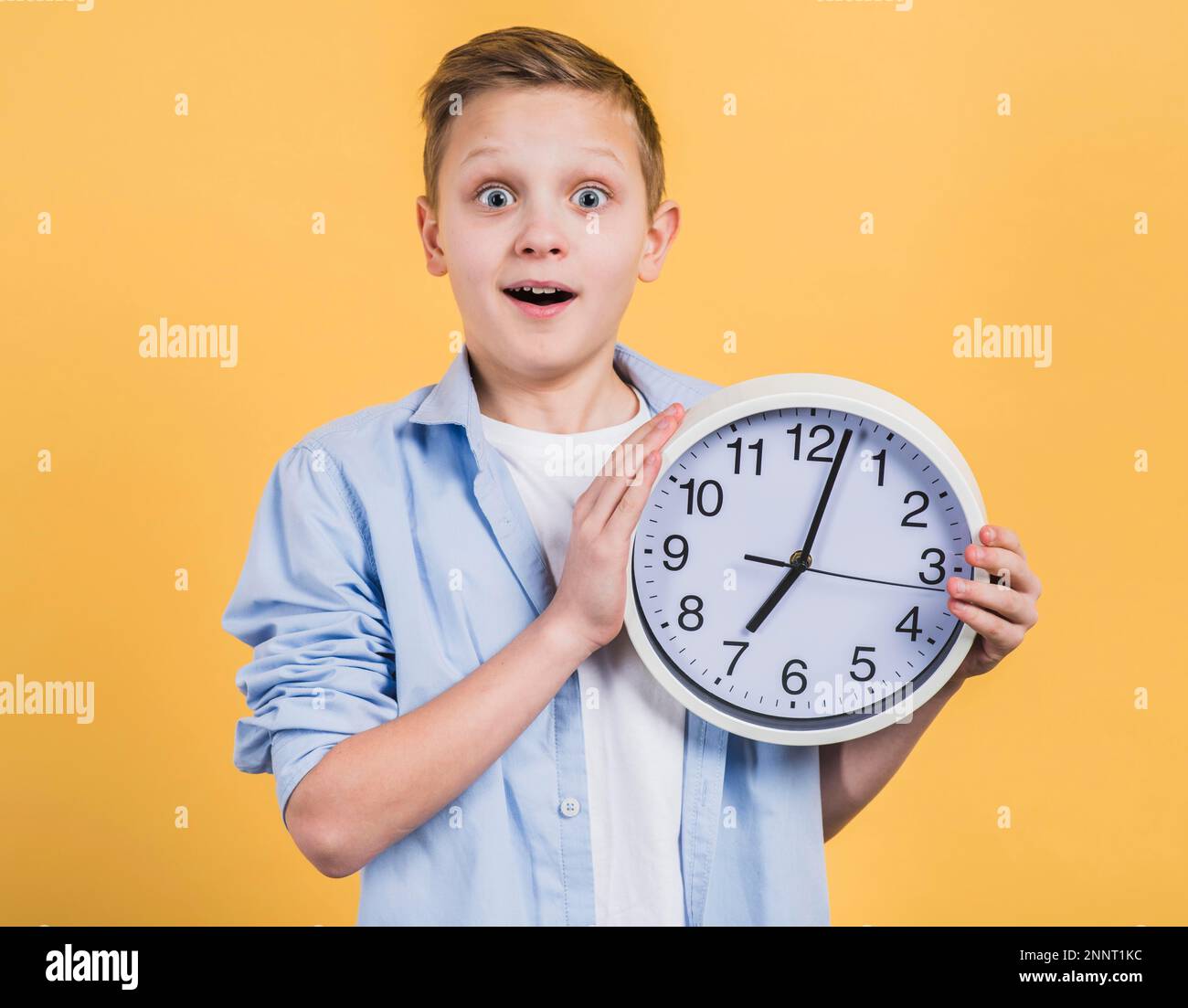 surprise smiling boy holding white clock hand looking camera against