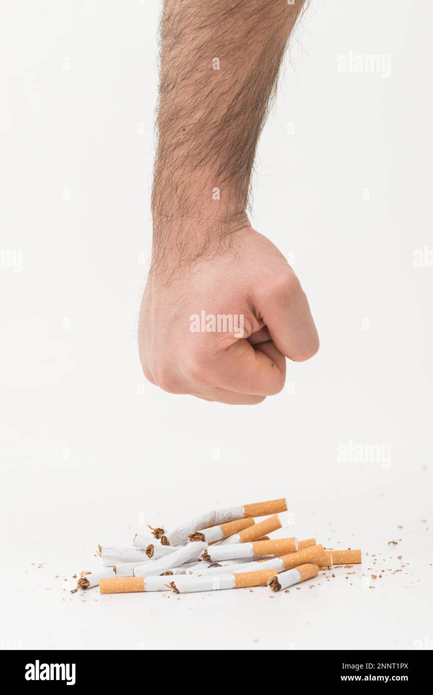 man s hand giving punch broken cigarettes isolated white backdrop Stock Photo