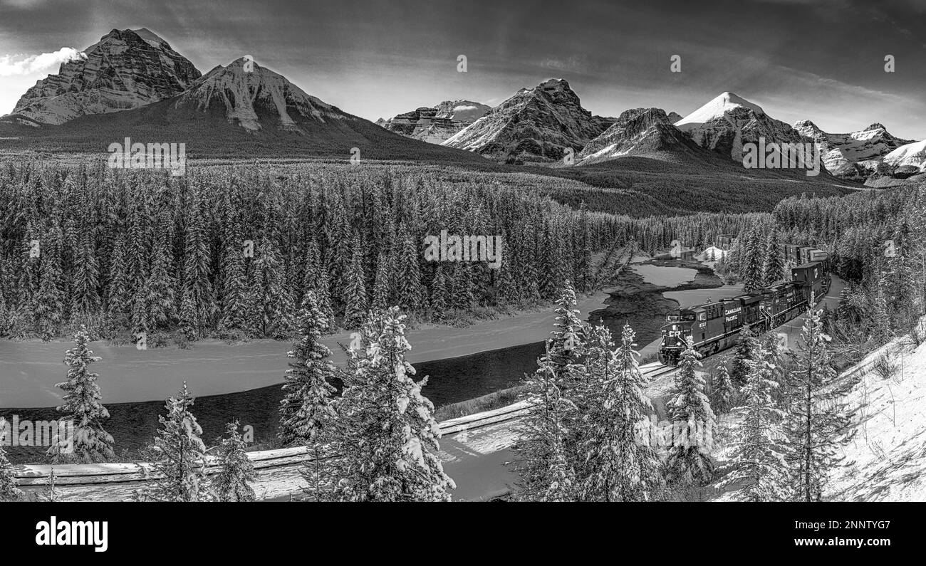 Train moving along Morants Curve and Bow River with mountain range in background, Lake Louise, Alberta, Canada Stock Photo