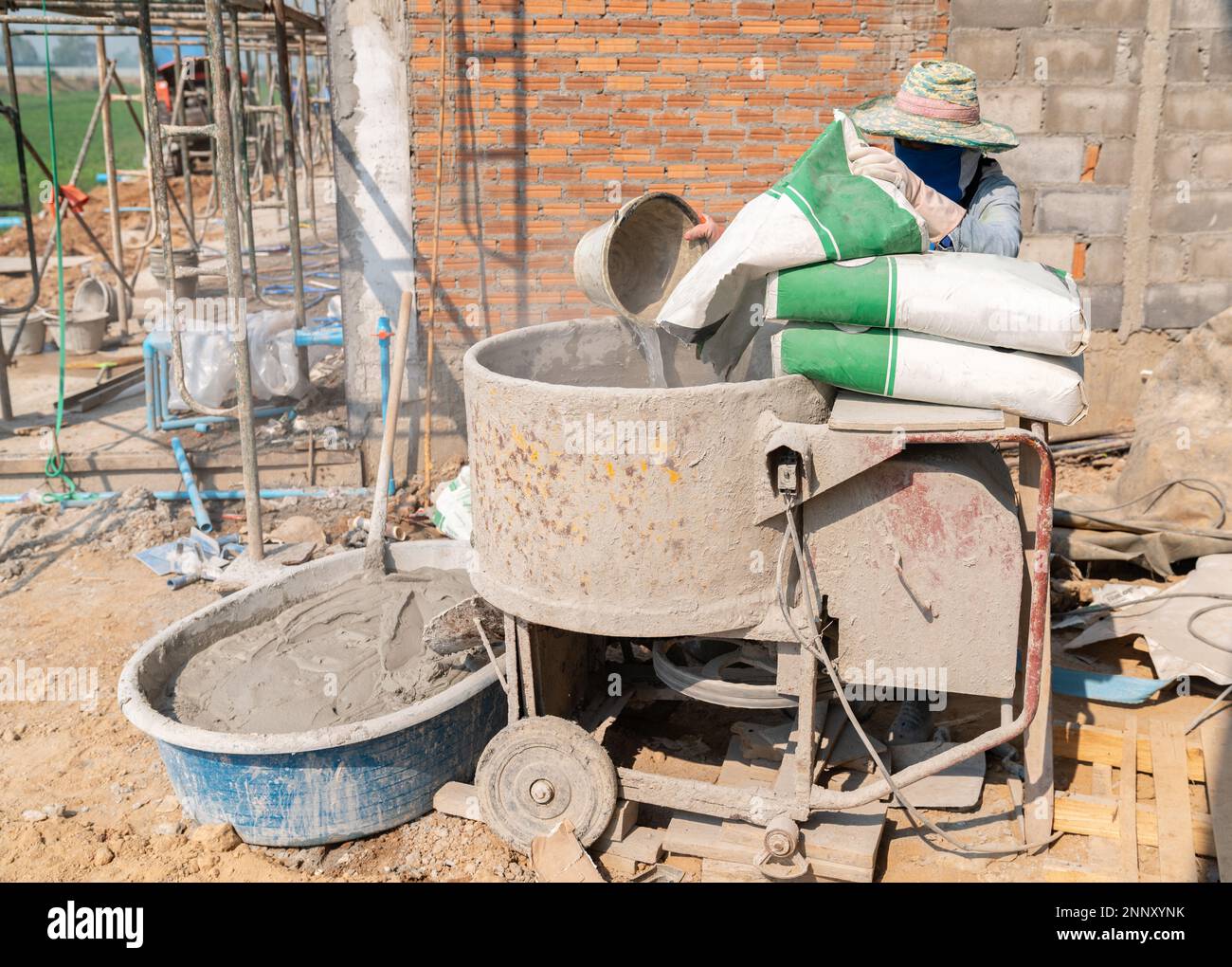 Builder working with a bucket in his hands loads a concrete mixer.orange concrete mixer prepares cement mortar Stock Photo