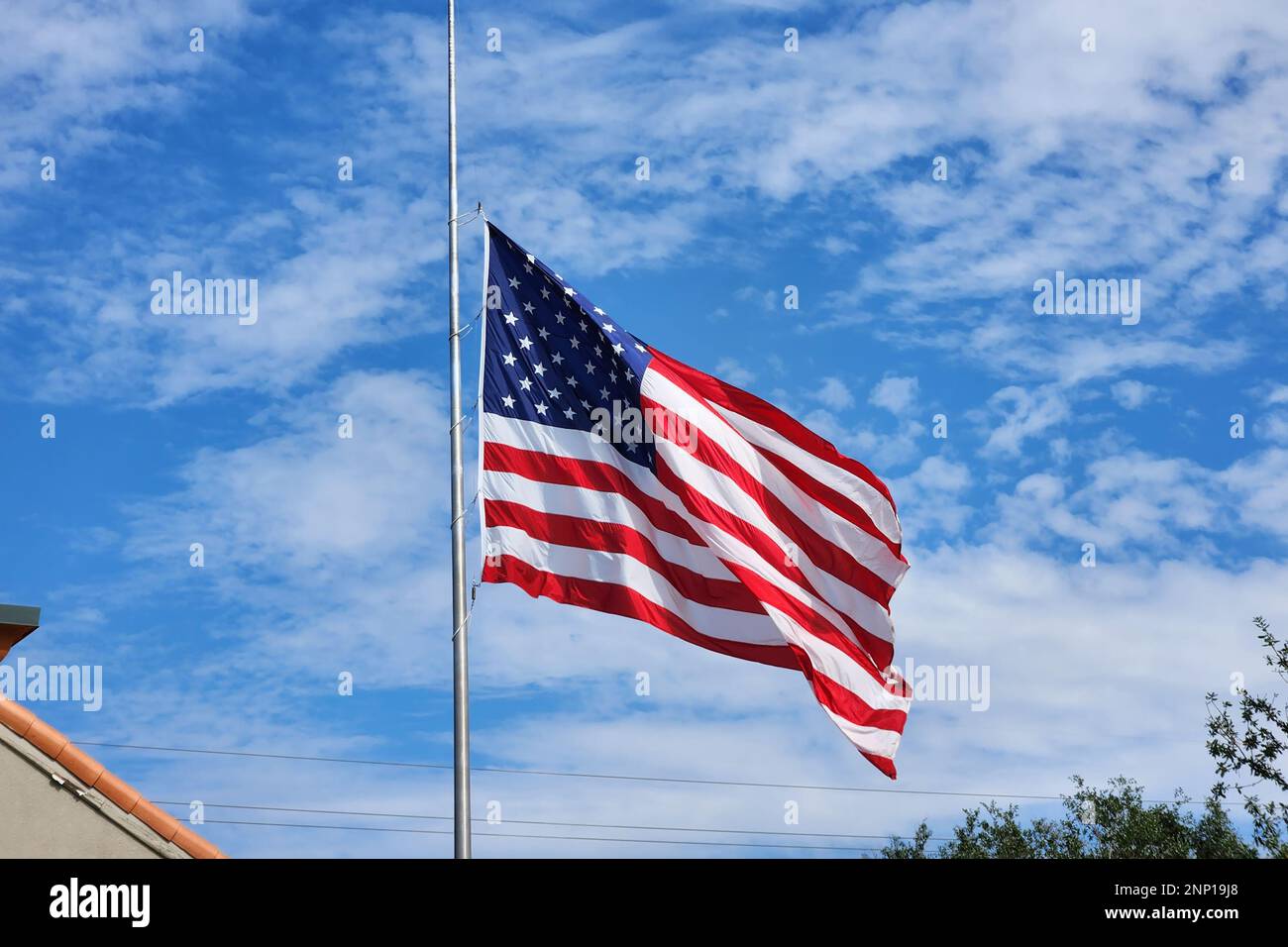 USA national flag waving lowered to half mast on wind against blue sky