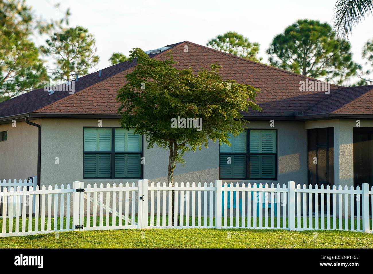 White vinyl picket fence on green lawn surrounding property grounds for backyard protection and privacy. Stock Photo