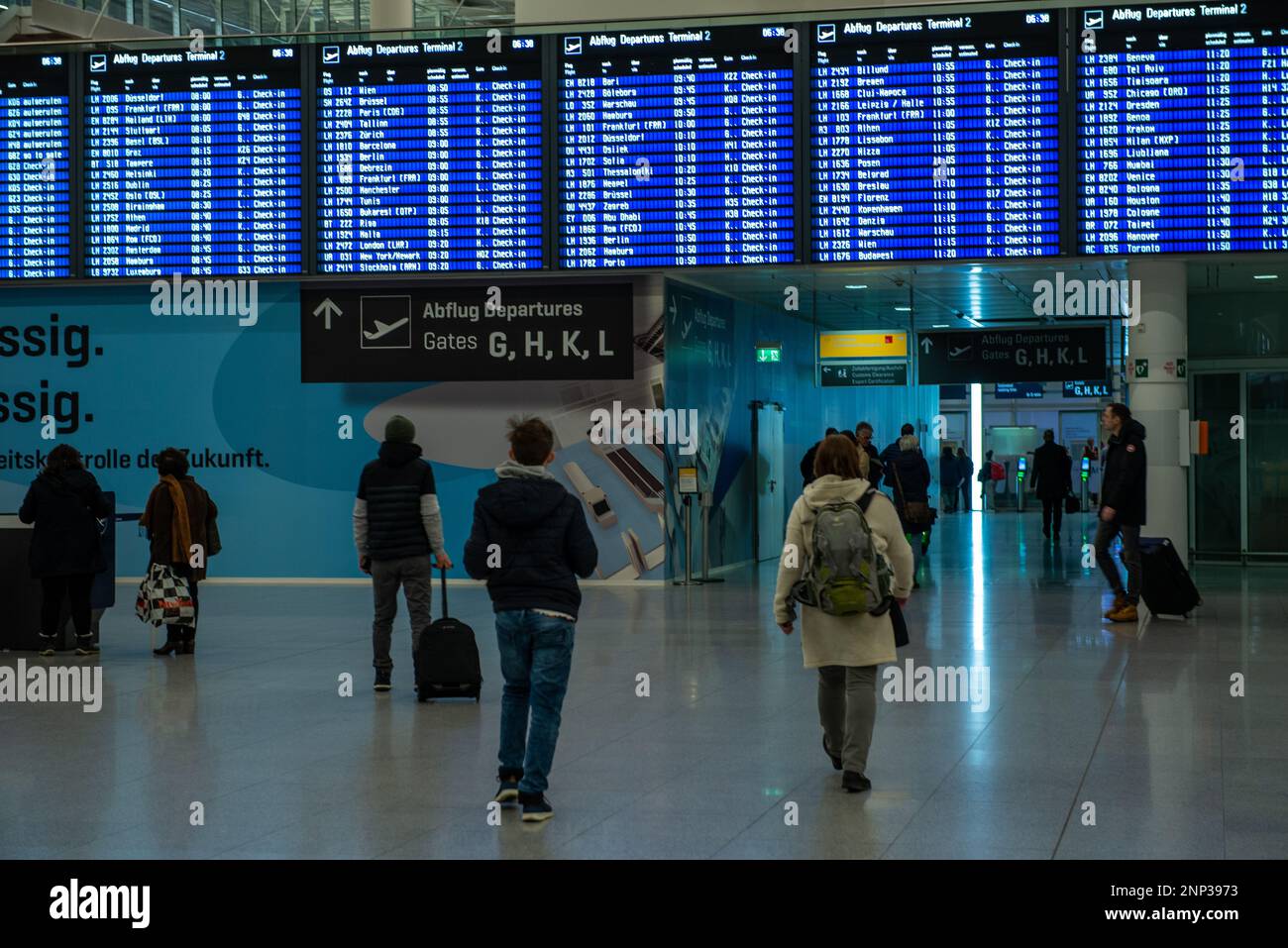 Munich,Germany- February 20,2023: Passengers walk under a flight departures board and a sign in germany indicating departure gates at Munioch airport. Stock Photo