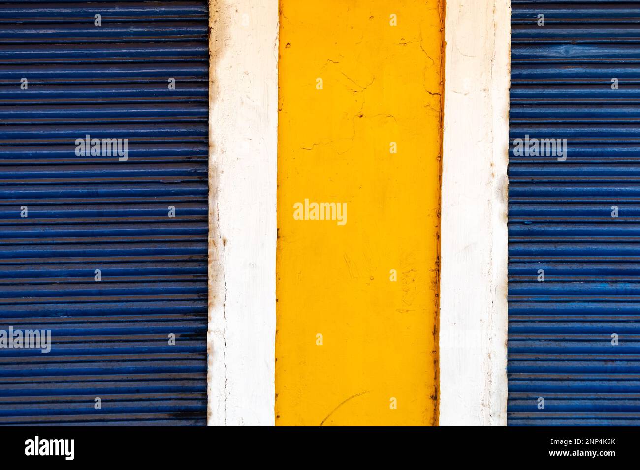 Abstract colorful geometric detail of a section of a wall painted yellow between blue shutters of a shop in Panjim in Goa. Stock Photo