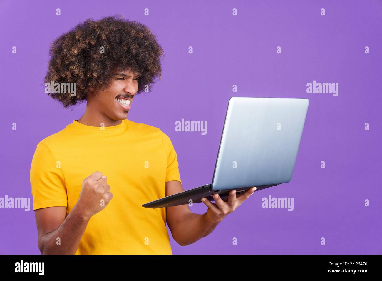 African man with curly hair celebrating while using a laptop Stock Photo