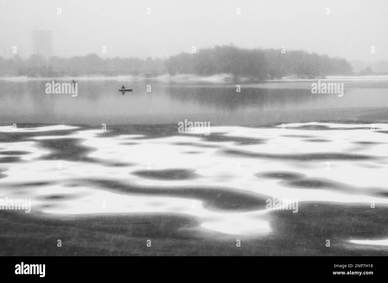 Snow storm on the first ice of the lake walking in a circle with people, and the trees on the shore, the fisherman's boat and foggy. Stock Photo