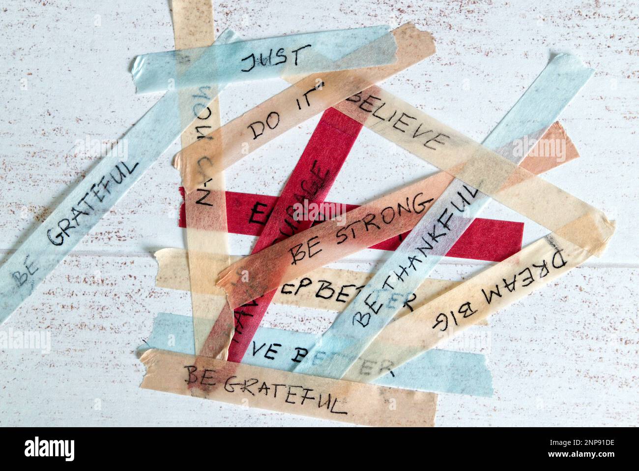 mixed up motivational messages handwritten on colorful washi tape against white wooden