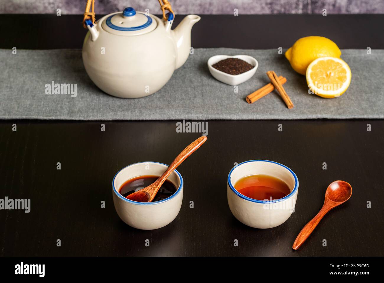 Two cups of tea, one green and one red in the foreground, in the background a teapot with lemons, pieces of cinnamon and ground tea. Stock Photo