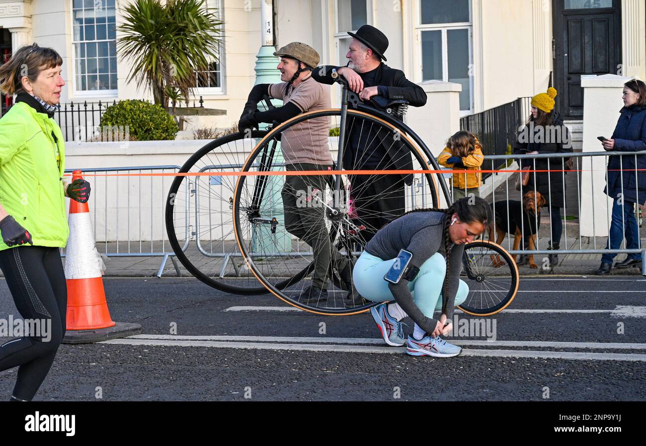 Brighton UK 26th February 2023 - Penny farthing riders watch as thousands of runners take part in the 33rd Brighton Half Marathon on a bright morning along the South Coast . Over ten thousand runners are expected to take part helping to raise money for various charities: Credit Simon Dack / Alamy Live News Stock Photo