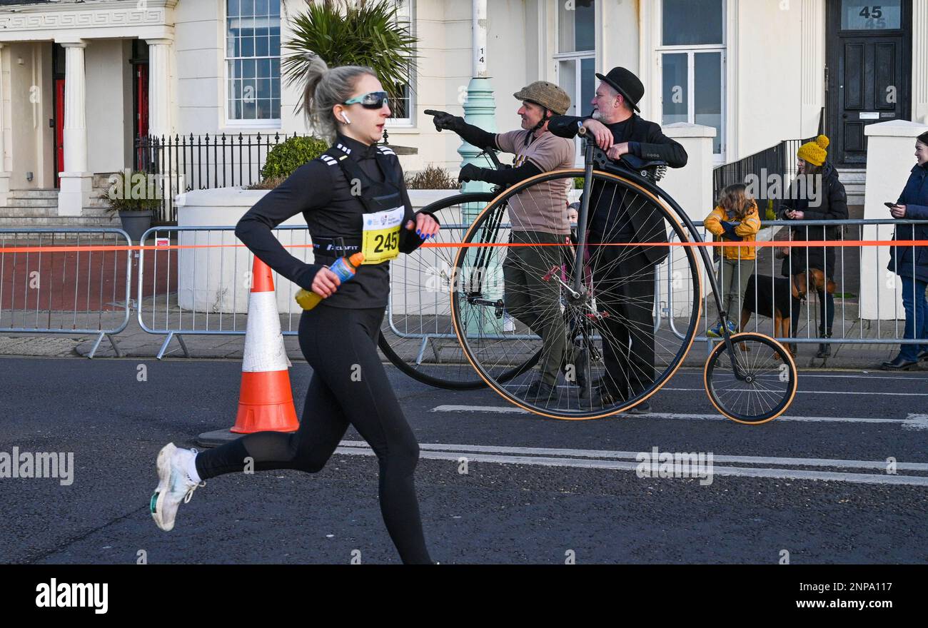 Brighton UK 26th February 2023 - Penny farthing riders watch as thousands of runners take part in the 33rd Brighton Half Marathon on a bright morning along the South Coast . Over ten thousand runners are expected to take part helping to raise money for various charities: Credit Simon Dack / Alamy Live News Stock Photo