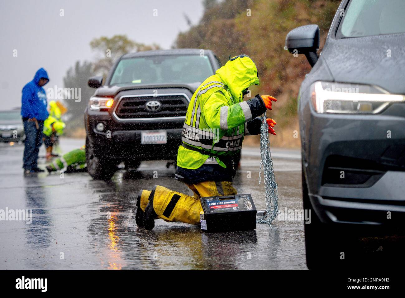 A snow chain installer assists a vehicle as snow chains are required on