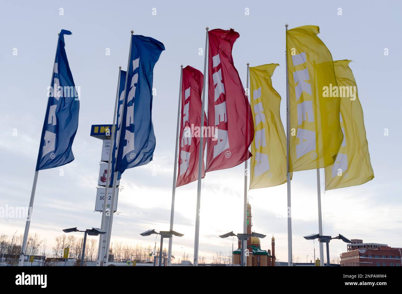 the flags of the store 'IKEA' in the wind in the winter with lights and a large advertising banner in the evening, at sunset Stock Photo