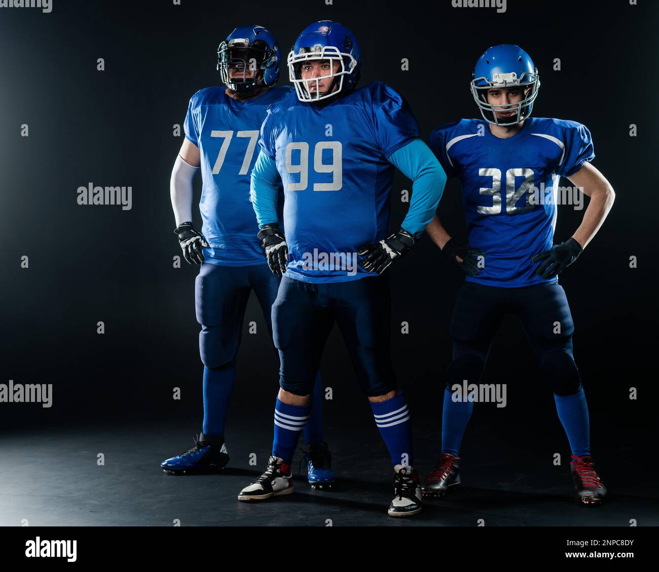 Portrait of three men in blue uniforms for American football on a black