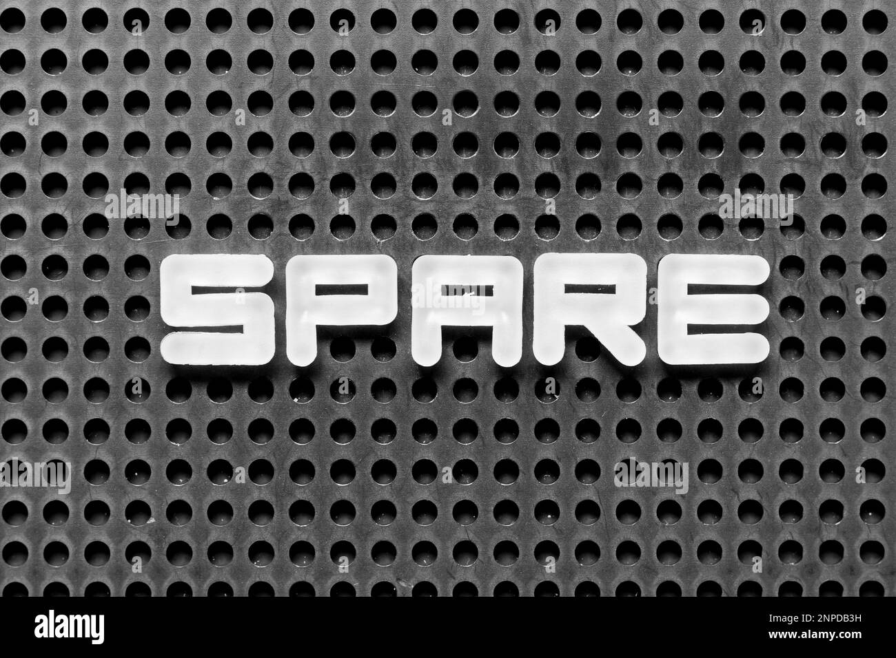 White alphabet letter in word spare on black pegboard background Stock