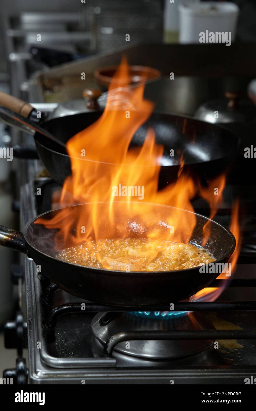 Pan on fire while flambeeing prawns for a delectable meal in a commercial kitchen, big skillet in flames while a skillful chef is cooking prawns Stock Photo