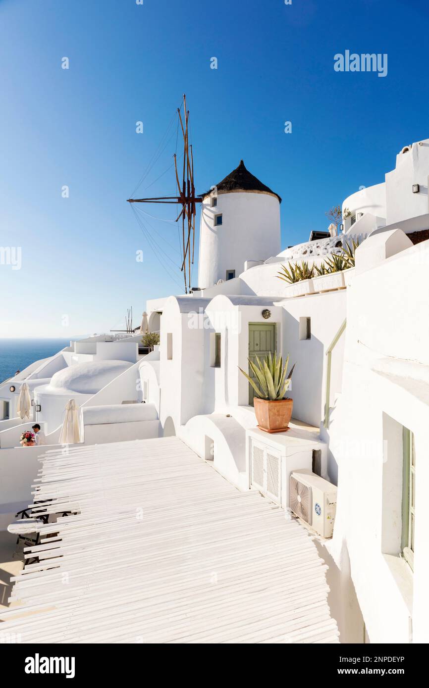 A view over the rooftops and towards a windmill against a blue sky in Oia. Stock Photo