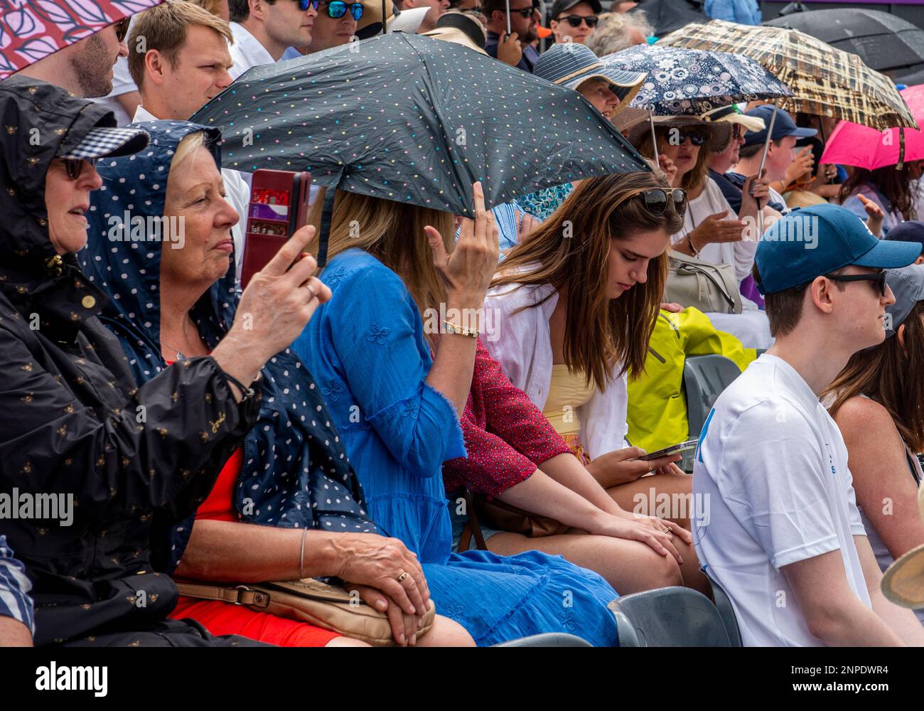 To keep the umbrella closer and shelter from the rain a lady accidentally gives the camera the finger at the Queen's Club tennis tournament. Stock Photo