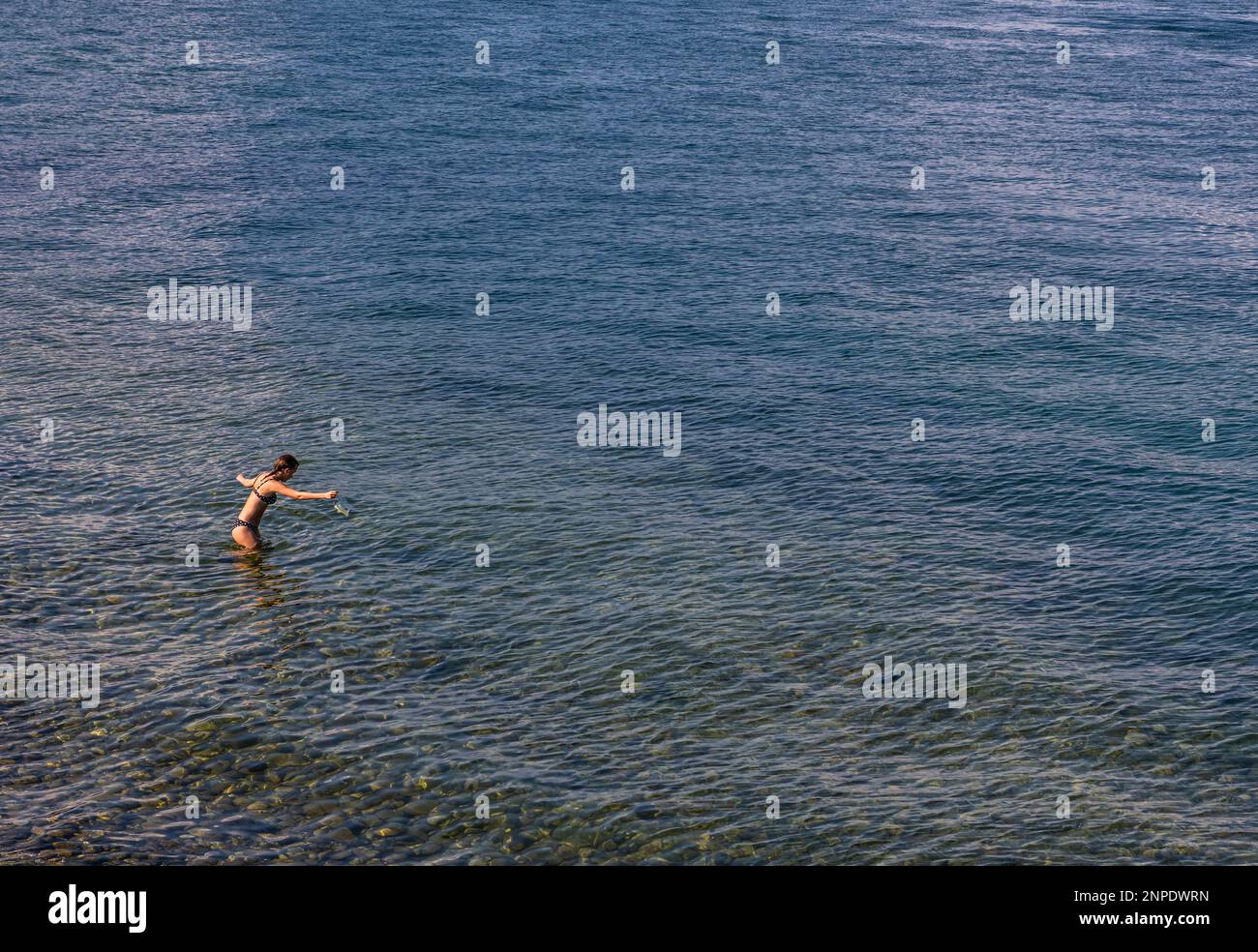 A young woman walks gingerly into the clean blue water of Lake Como. Stock Photo