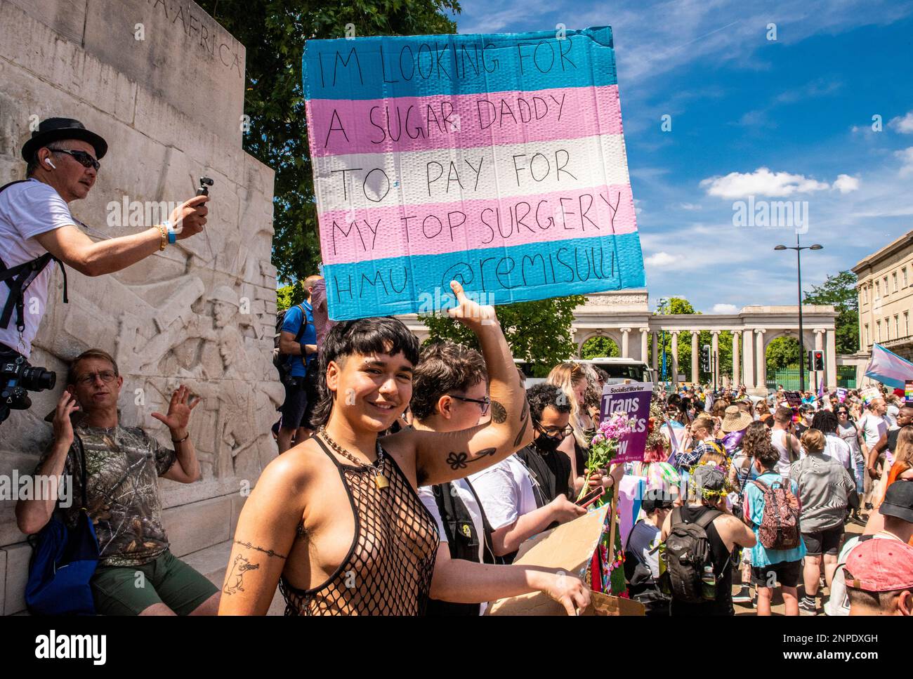 A member of the LGBTQ+ community smiles and holds a banner as they protest against the lack of rights and healthcare for transgender people. Stock Photo