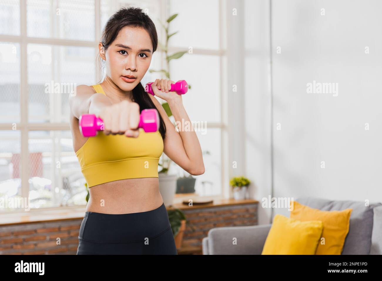 Sporty young woman raises dumbbell, young Asian female exercising with her weights in the living room Stock Photo