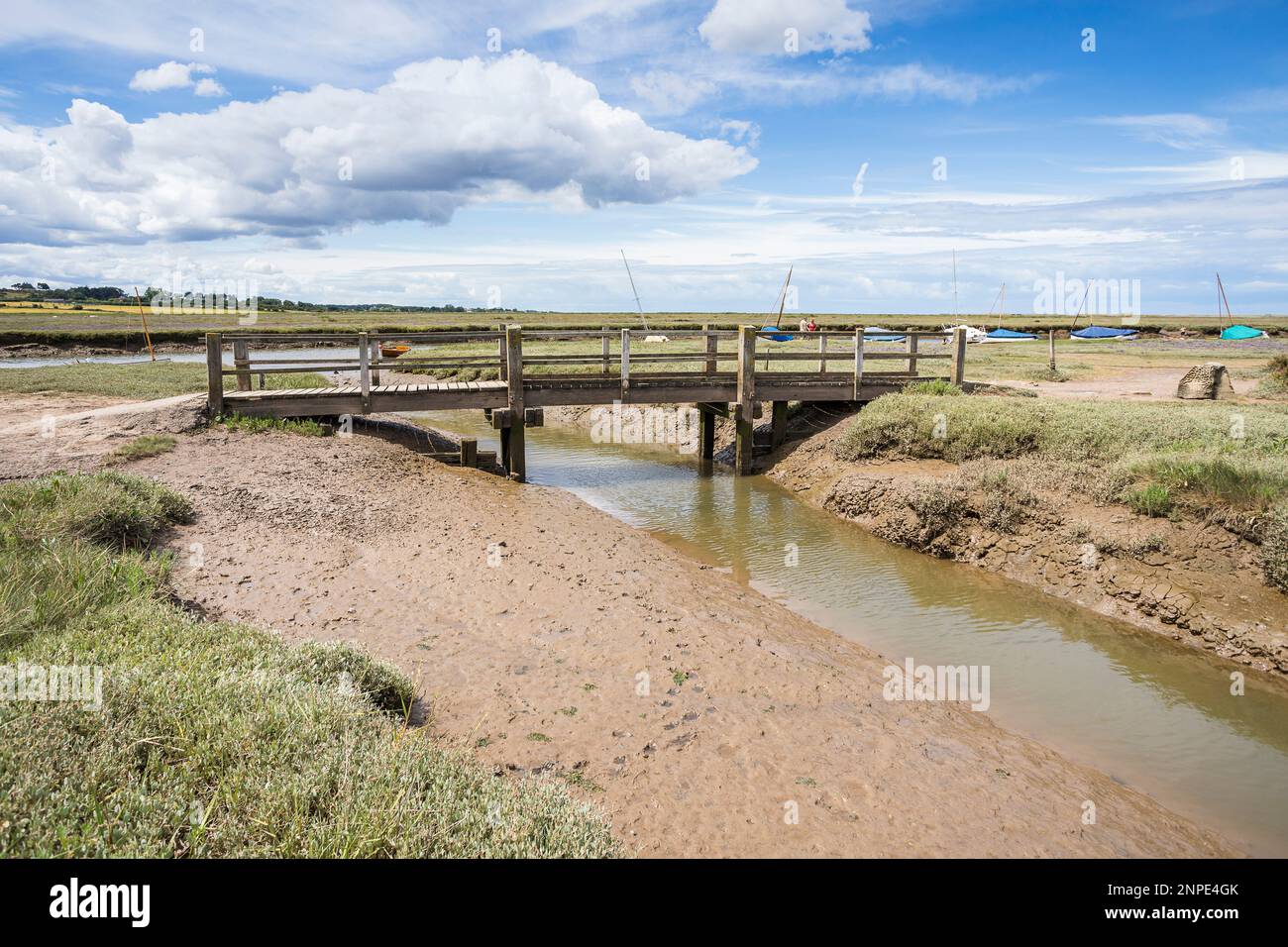 A wooden bridge spans a channel of water at low tide at Blakeney on the North Norfolk coast. Stock Photo