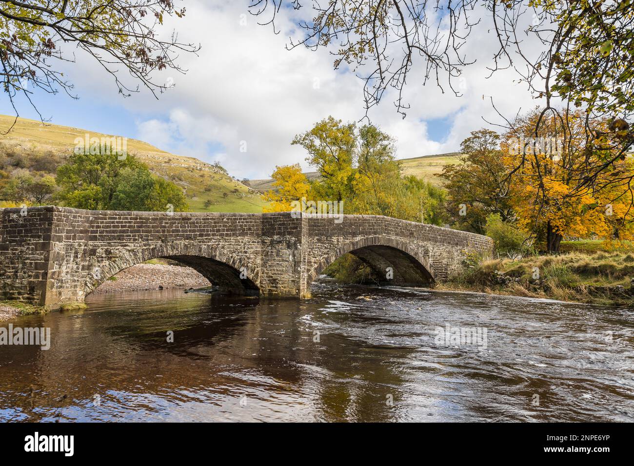 Colourful trees surround and frame the beautiful bridge which spans the River Wharfe in Bucken in the Yorkshire Dales. Stock Photo