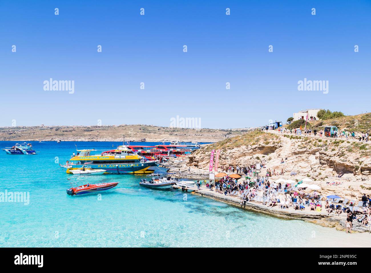 Tourists on the shore of the Blue Lagoon on Comino Island embarking and disembarking various types of boats. Stock Photo