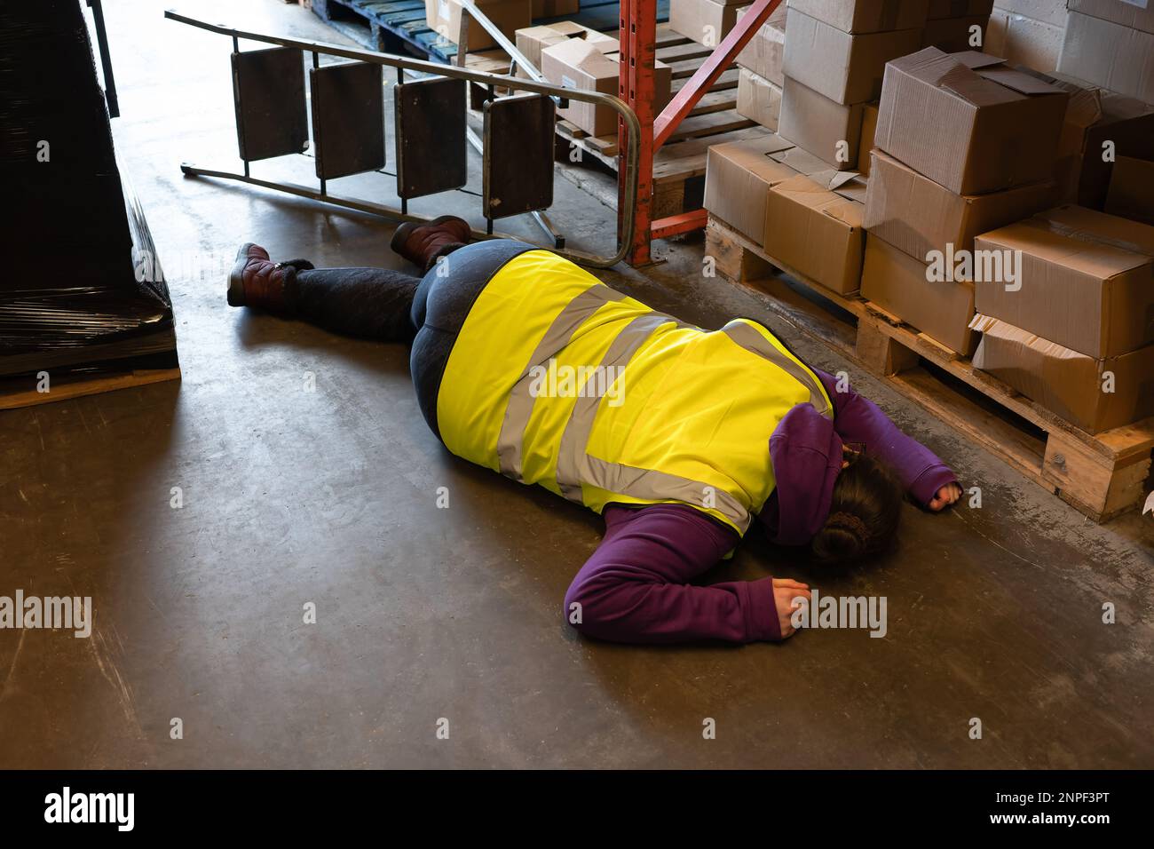 Accident in the work place, young woman lies injured after falling from step ladder onto the factory floor Stock Photo