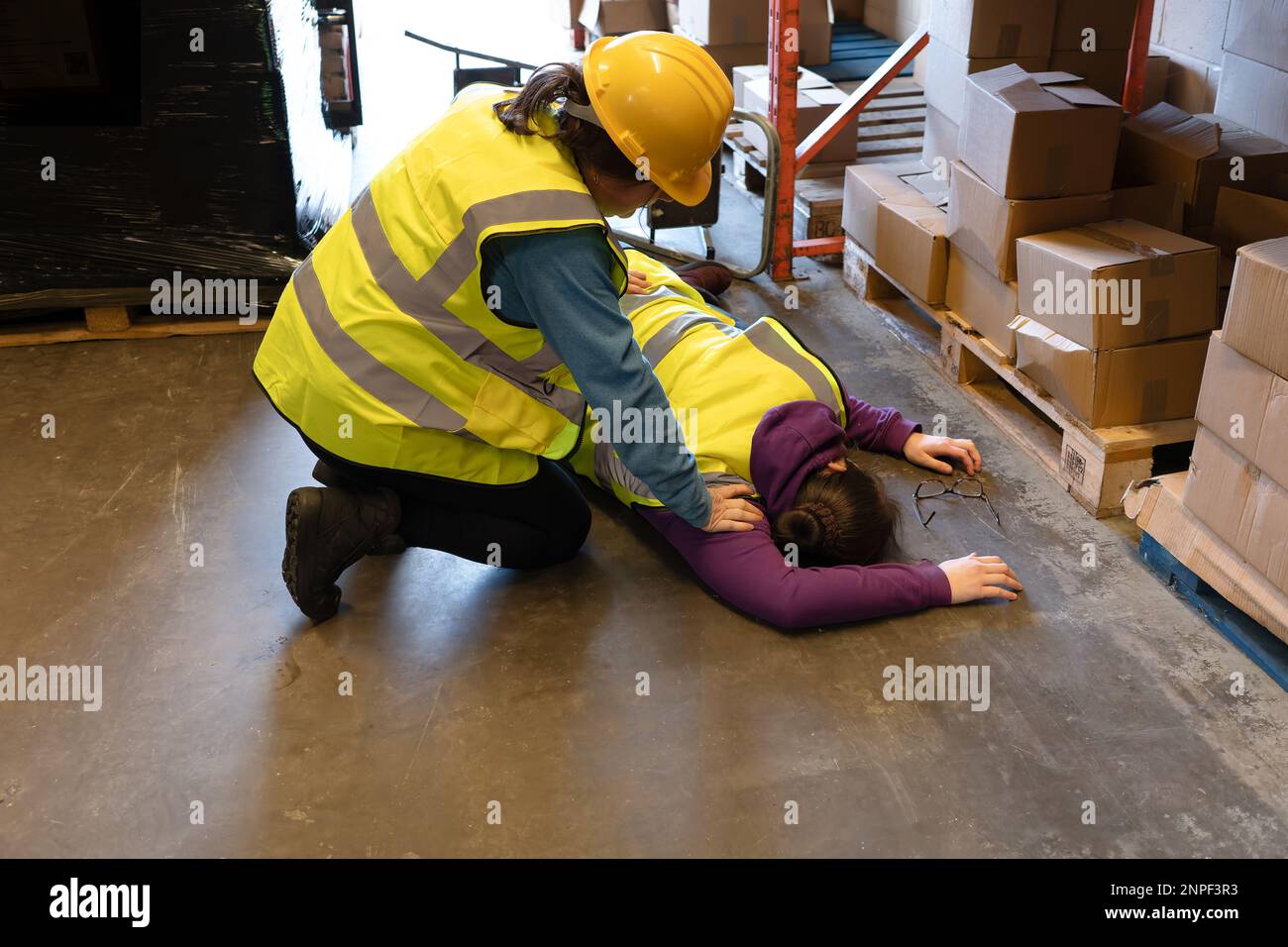 Accident in the work place ,young woman lies injured after falling from step ladder onto the factory floor second staff member assists Stock Photo