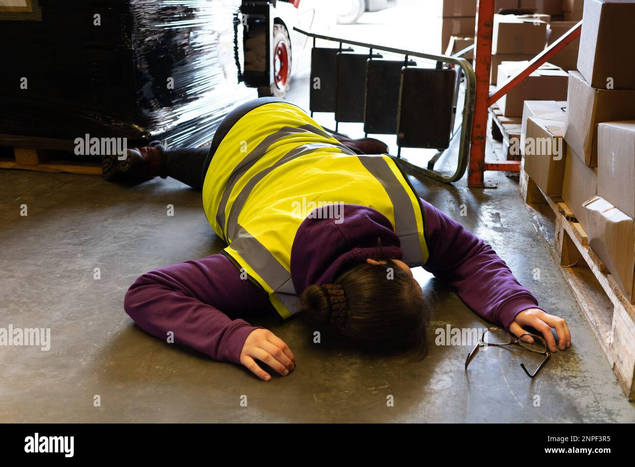 Accident in the work place, young woman lies injured after falling from step ladder onto the factory floor Stock Photo
