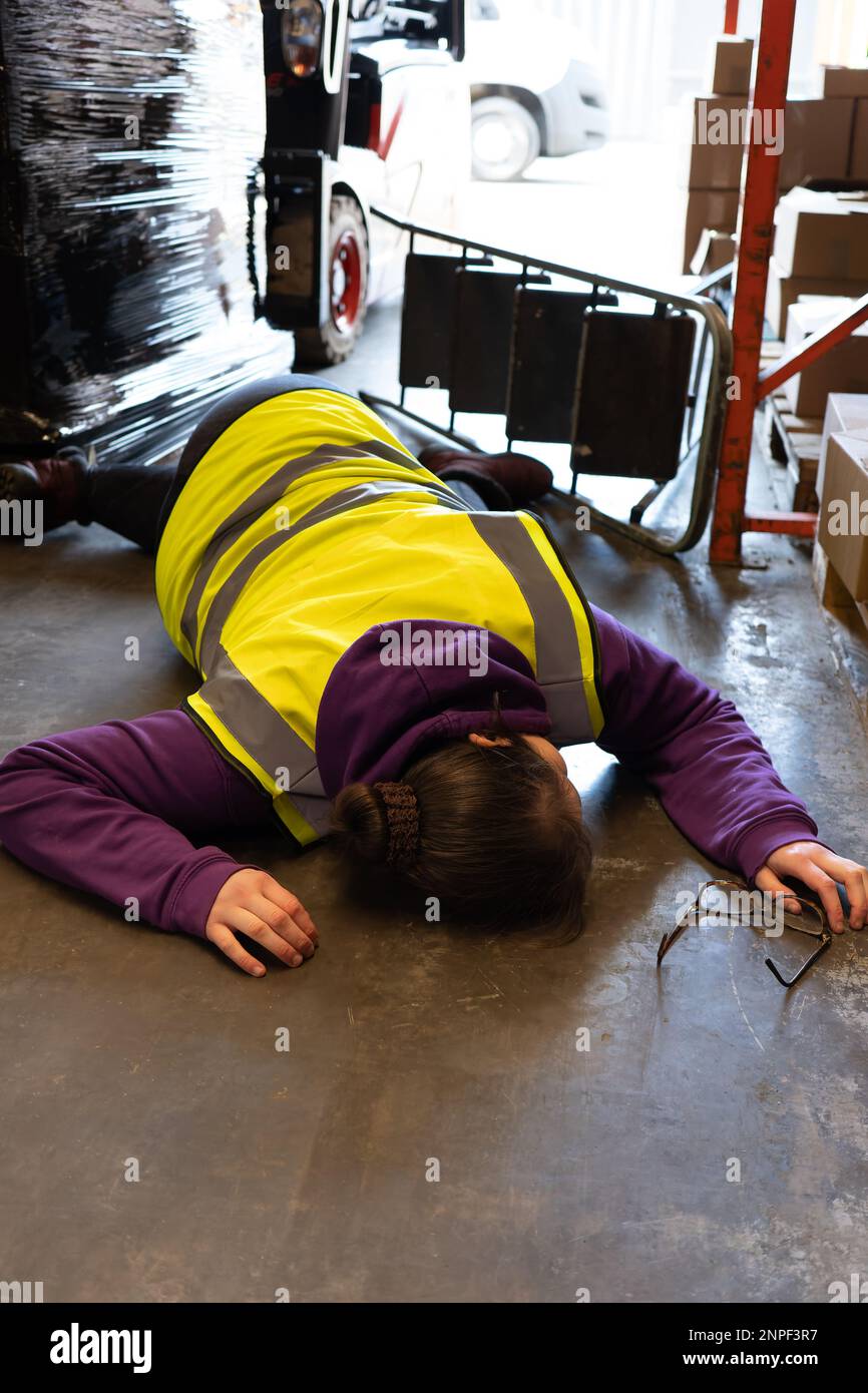Accident in the work, place young woman lies injured after falling from step ladder onto the factory floor Stock Photo