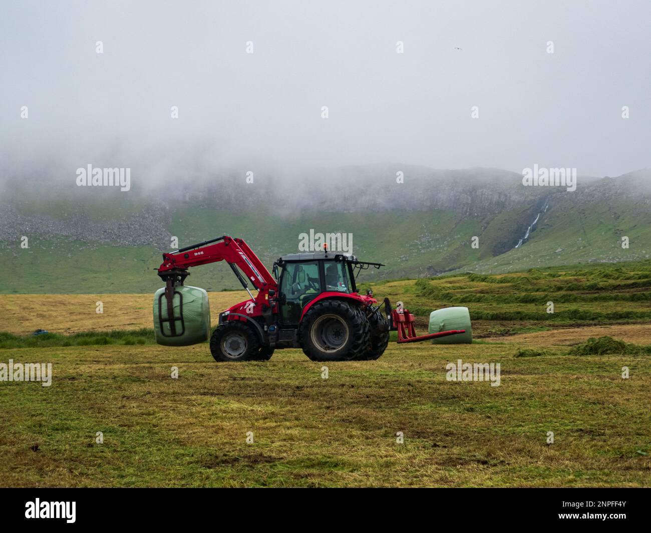 Norðradalur, Faroe Islands - July, 2021: Automated haymaking in the foggy hills above the Atlantic Ocean on Streymoy Island. Kingdom of Denmark. North Stock Photo