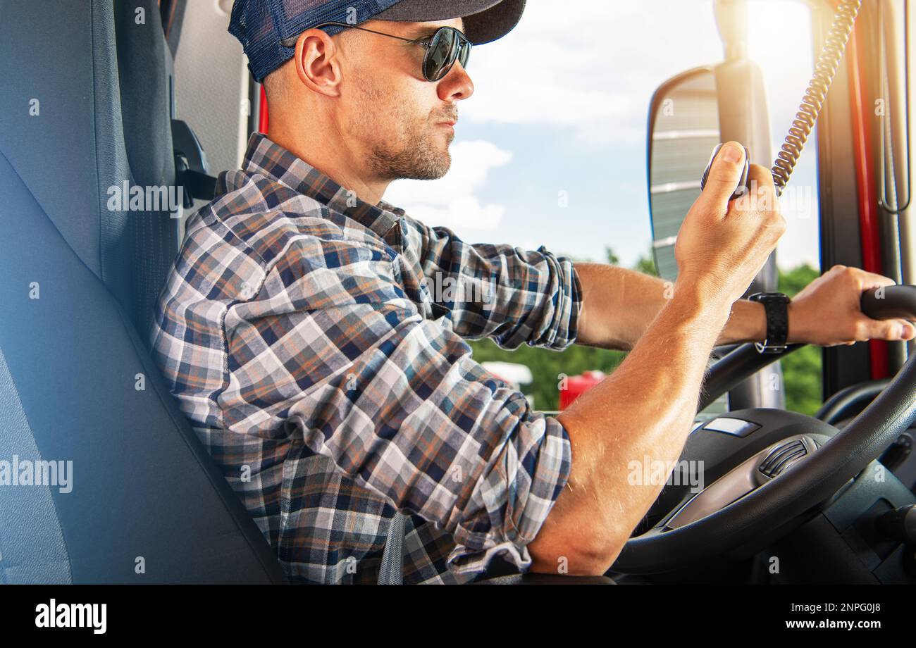 Commercial Trucker Driver in His 40s Behind the Truck Wheel Talking Over the Radio. CB Communication on the Road. Transportation Theme. Stock Photo