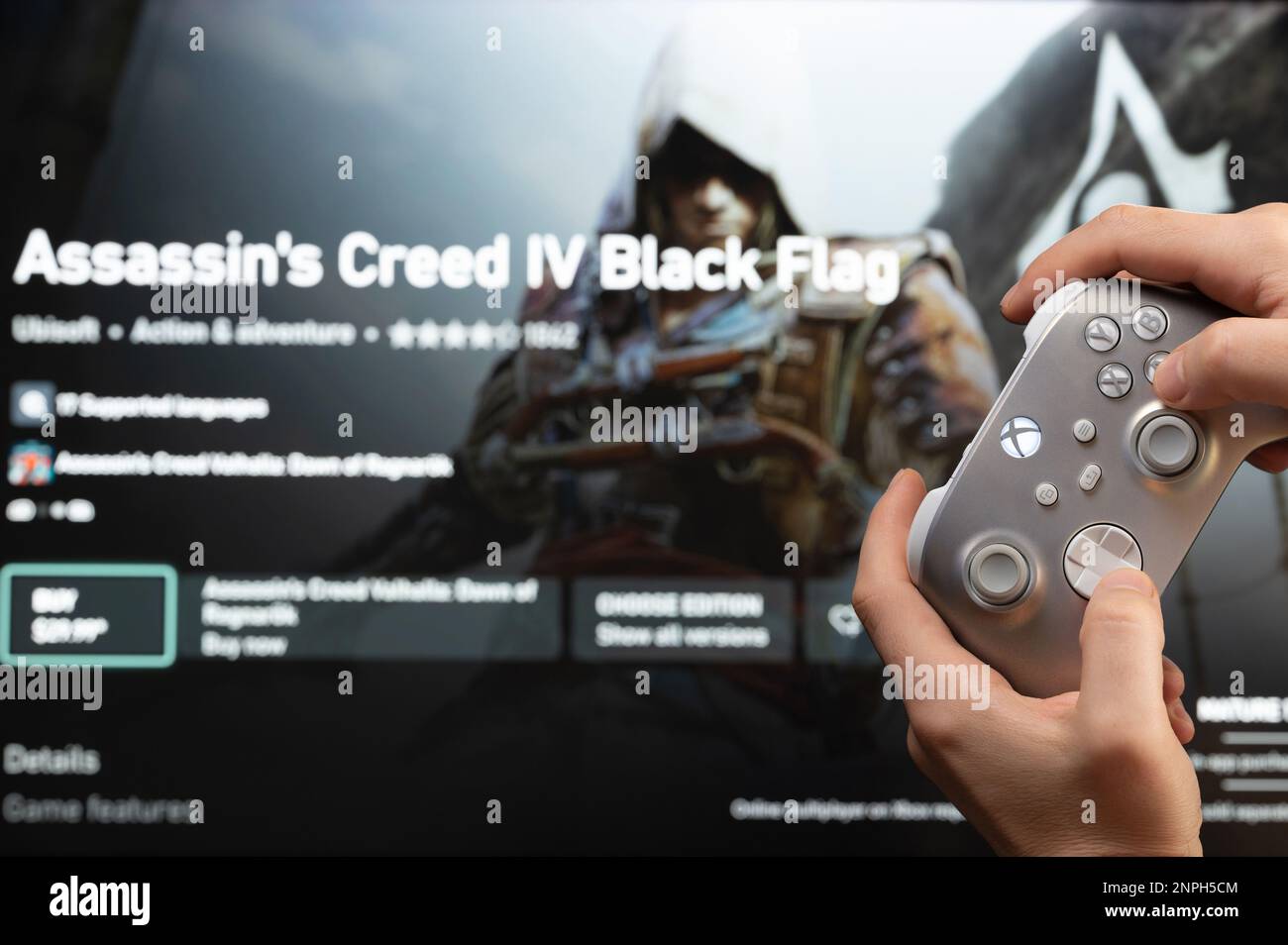 New york, USA - February 20, 2023: Buy new game Assassin's  Creed in online microsoft xbox store with gamepad controller in hand Stock Photo