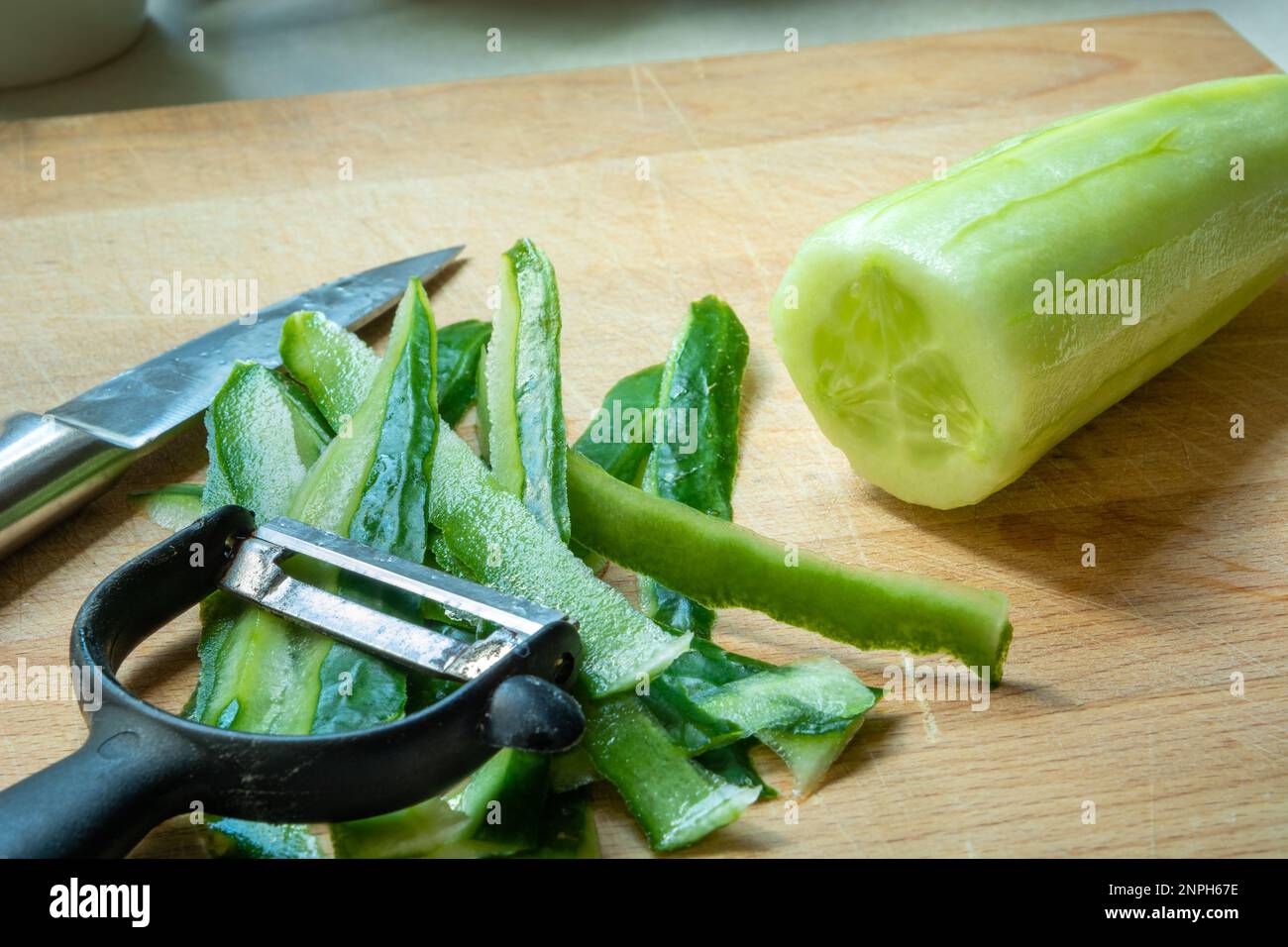Vegetable peeler and knife lying next to peeled green cucumber Stock